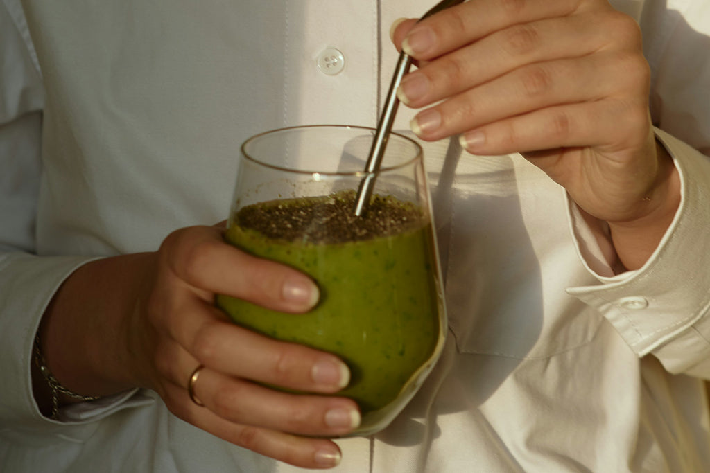 Female hands holding a glass of green smoothie with eco-friendly reusable metallic straw